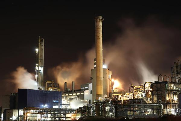 Factory at night with bright lights, chimneys and smoke