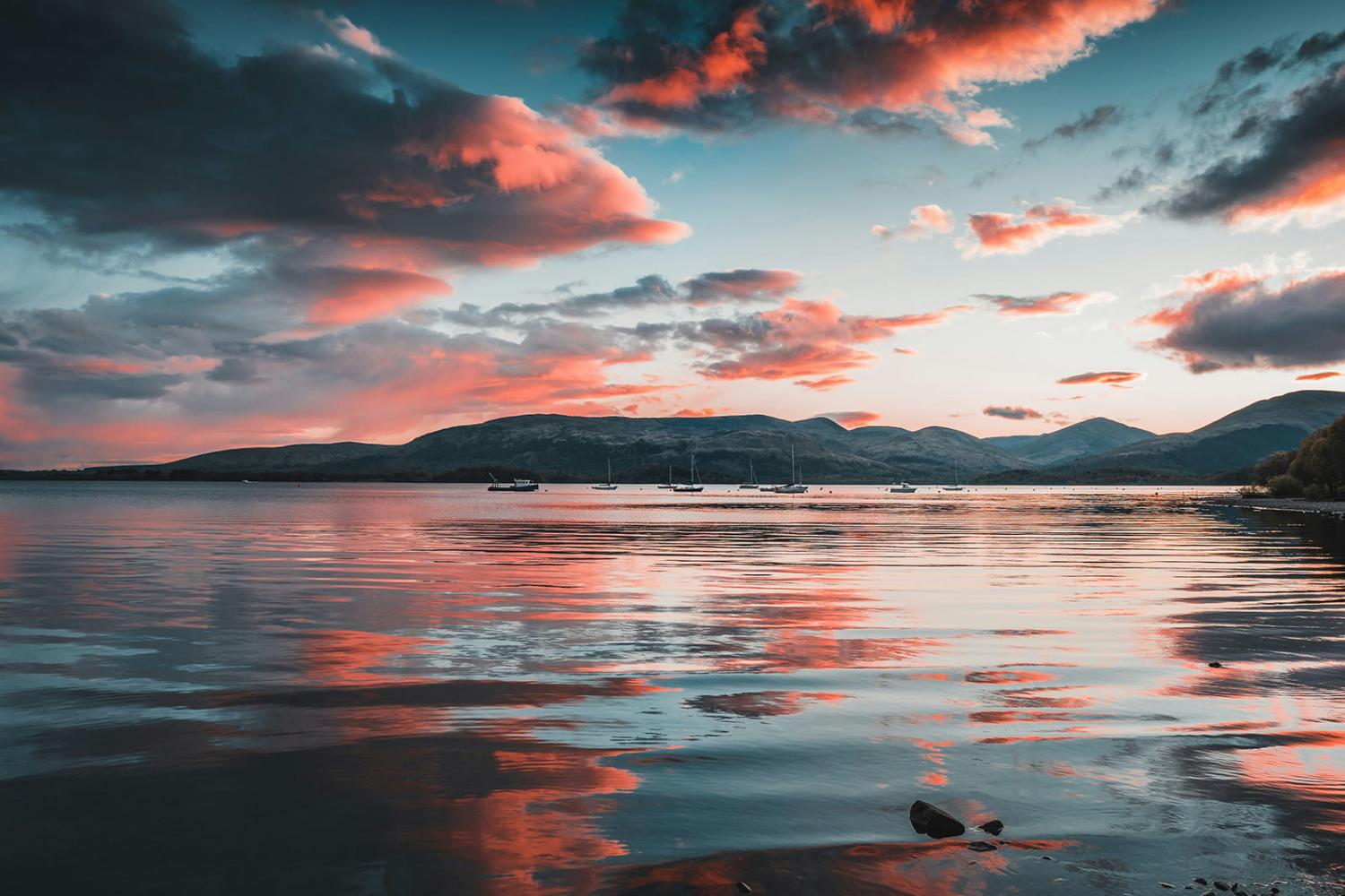 Peaceful landscape with water, boats and mountains in the distance and a big sky.