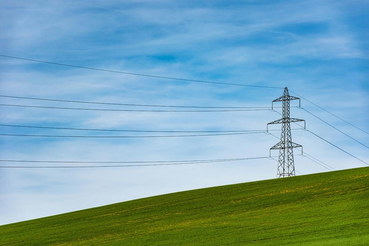 Electricity pylon and overhead wires against a blue sky above a green field
