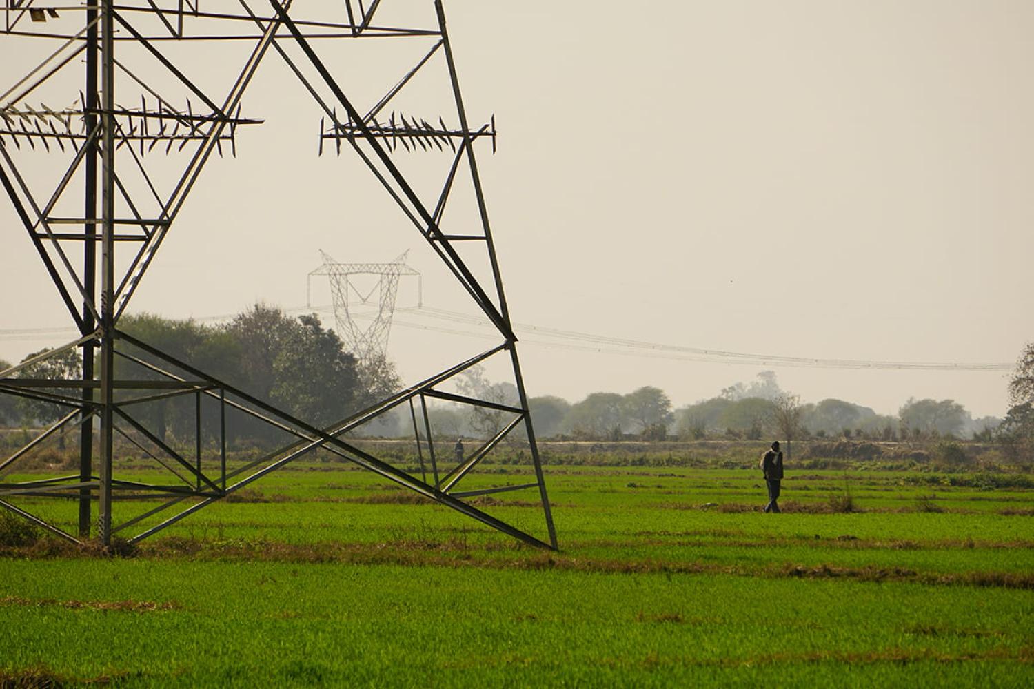 Electricity pylons in a lush green field with a person walking past