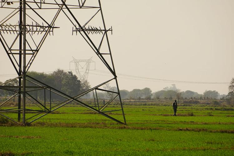 Electricity pylons in a lush green field with a person walking past